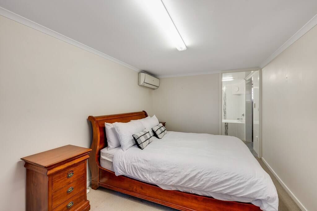 Une chambre à coucher avec un lit en bois, du linge de lit blanc, une commode en bois et un climatiseur fixé au plafond.