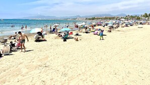 Una playa concurrida con gente tomando el sol y nadando.