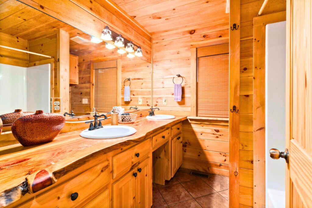 Un baño estilo cabaña de madera con dos lavamanos, un espejo grande y un mueble de madera.