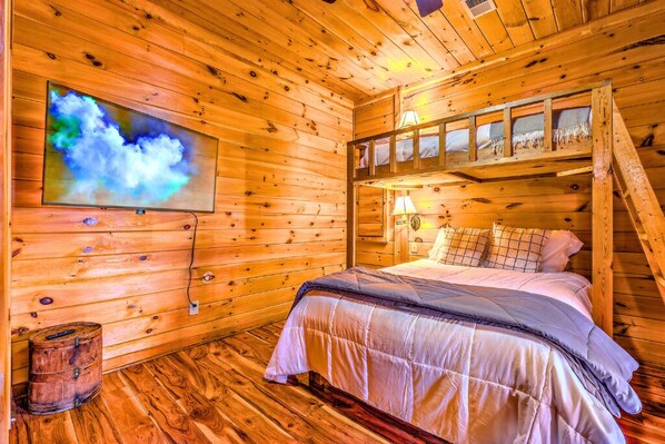 A wooden cabin room with a bed, a television, a ladder, and a wooden barrel.