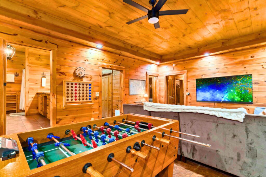 A wooden-floored room with a foosball table, a television, and a ceiling fan.