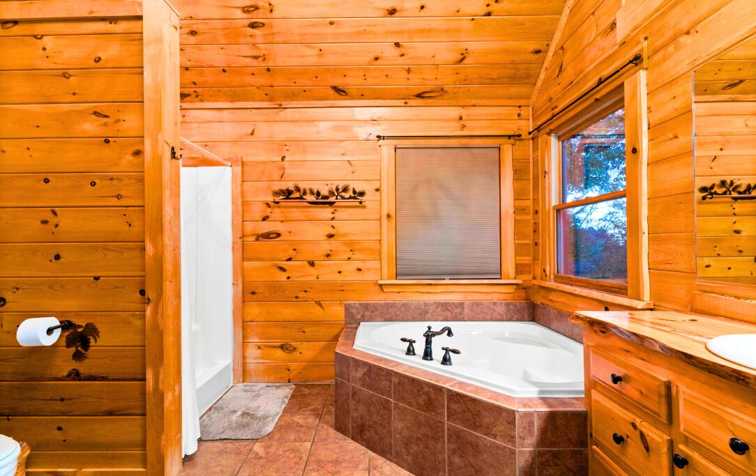 A wooden cabin bathroom with a bathtub, a toilet, and a window.