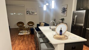 Een moderne keuken met een centraal eiland, barkrukken, een koelkast en een eethoek met stoelen en een vloerkleed.