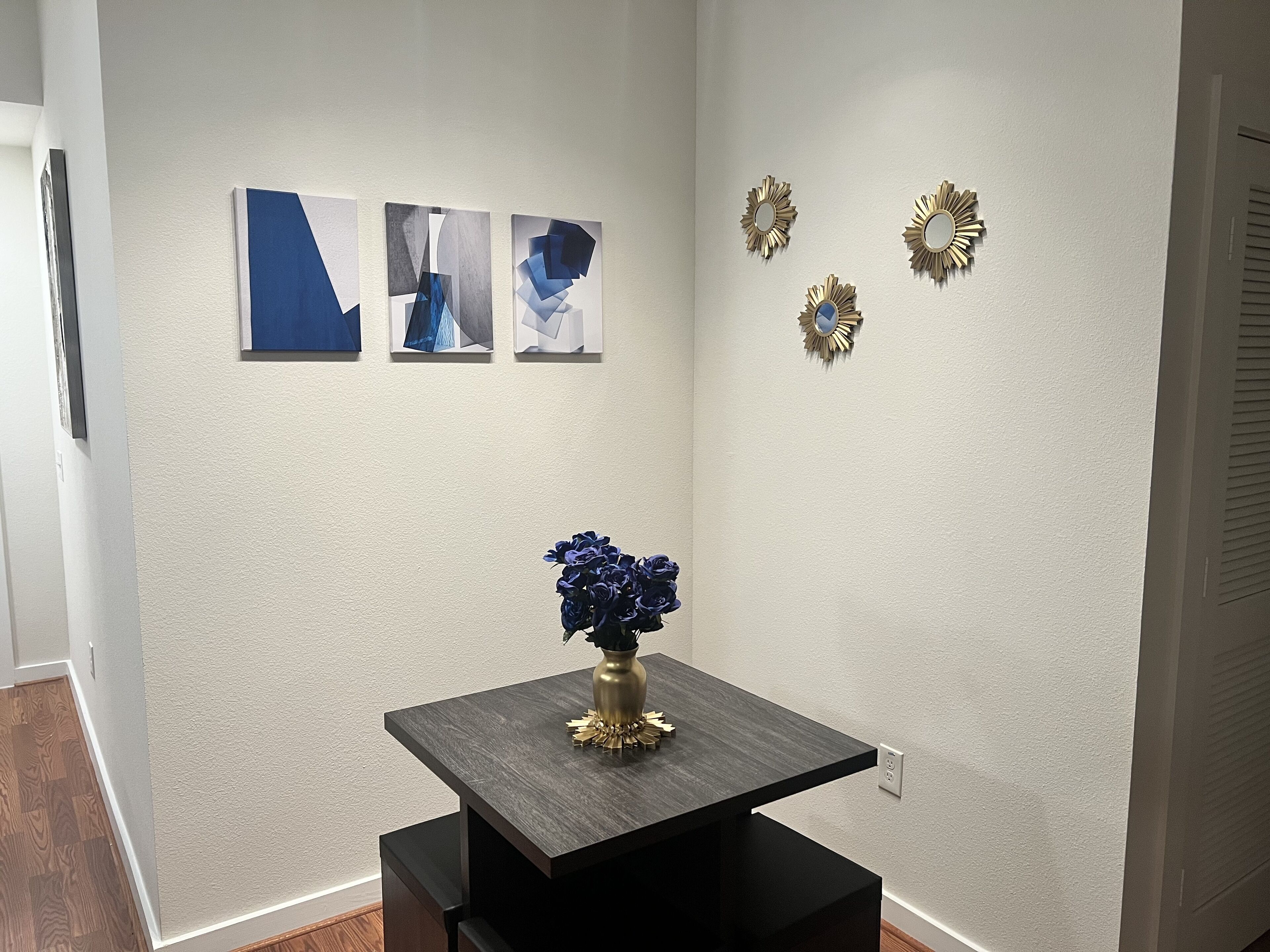 A hallway with a dark wooden table, a vase with blue flowers, and three abstract paintings on the wall.