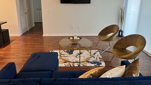 Een woonkamer met een blauwe bank, een glazen salontafel en twee stoelen.