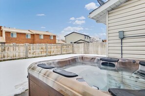 Un jacuzzi en un patio trasero con una valla de madera, una casa y un cielo despejado.