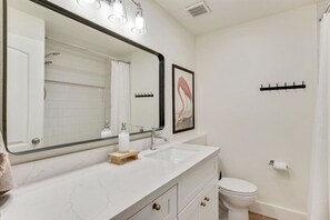 Un baño con un espejo grande, un lavabo, un inodoro y una ducha.