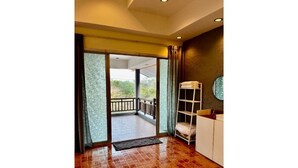 A room with a red-tiled floor, a white wardrobe, a small white shelf, and a view of a balcony with a railing. - Seaside home for families and furry friends! (Pranburi)
