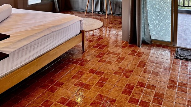 A hotel room with a bed, a TV on a stand, a large window with curtains, and a tiled floor. - Seaside home for families and furry friends! (Pranburi)