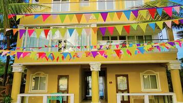 A two-story building with a yellow facade, balconies, and colorful triangular flags.