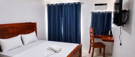 Habitación de hotel con cama de madera, un escritorio con silla, televisión y ventana con cortinas.