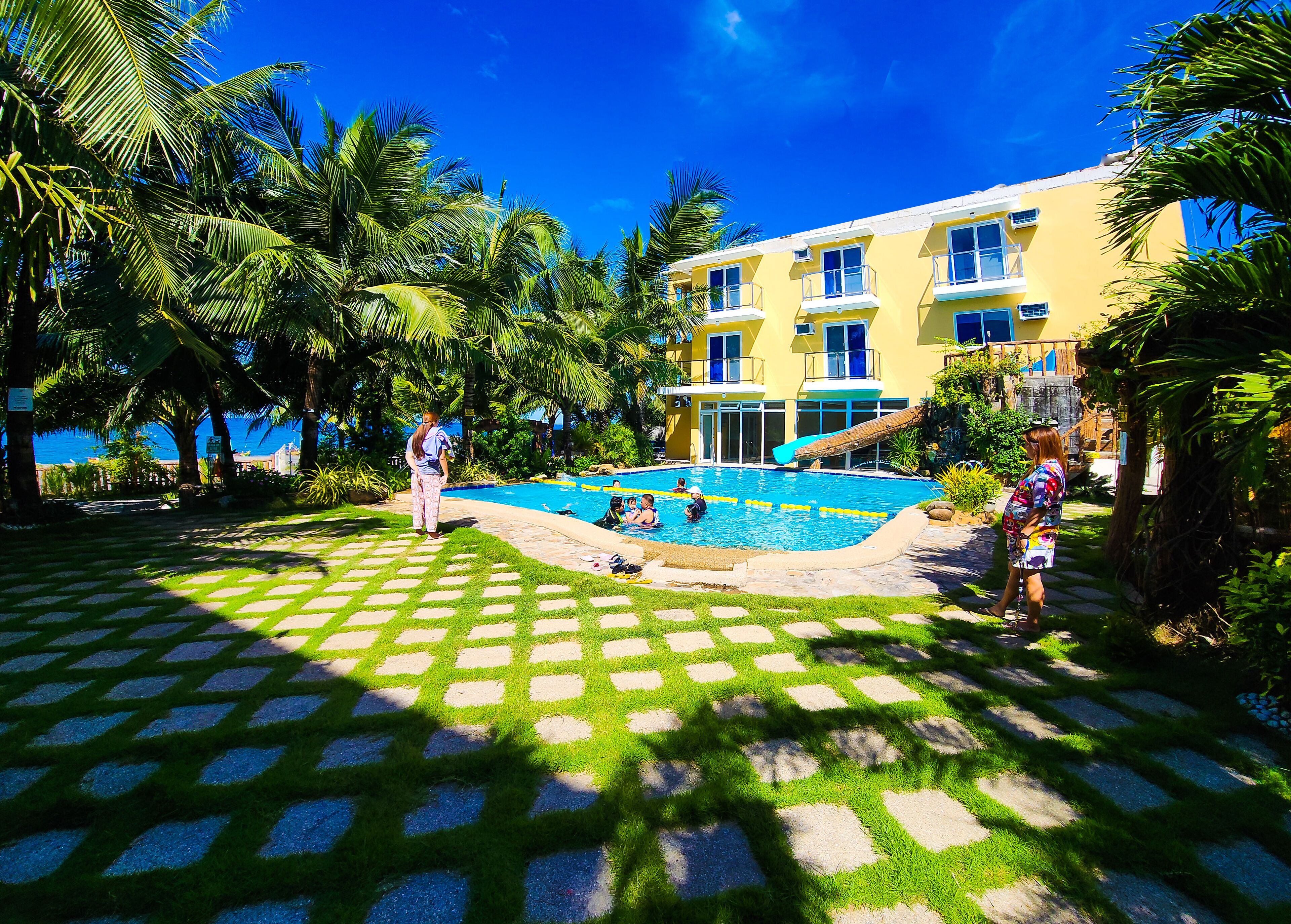 A pool area with a clear view of the pool, surrounding palm trees, and a building with multiple windows.