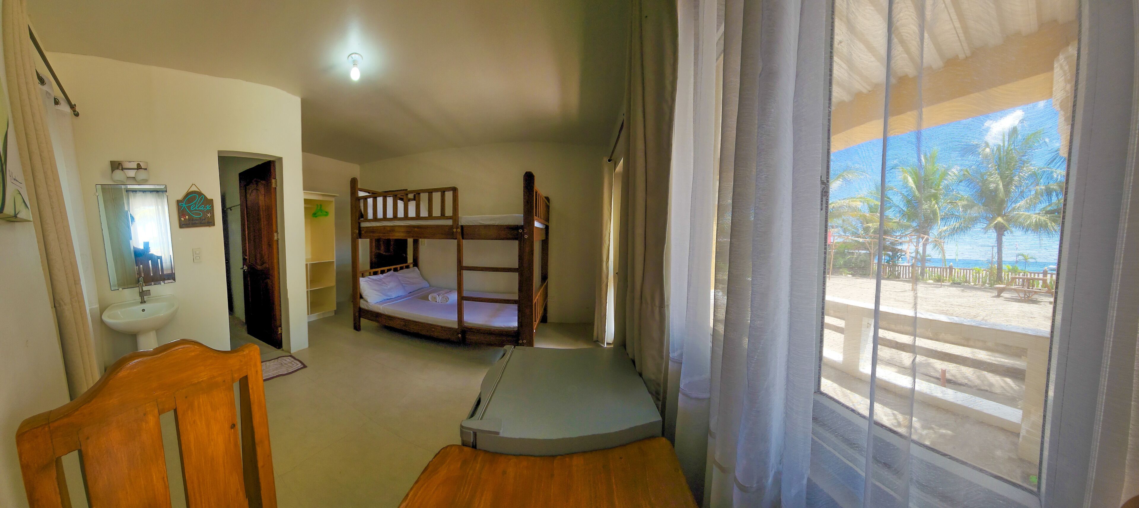 Una habitación con una cama individual superpuesta, un escritorio pequeño, una silla, un lavabo y vista a la playa por la ventana.