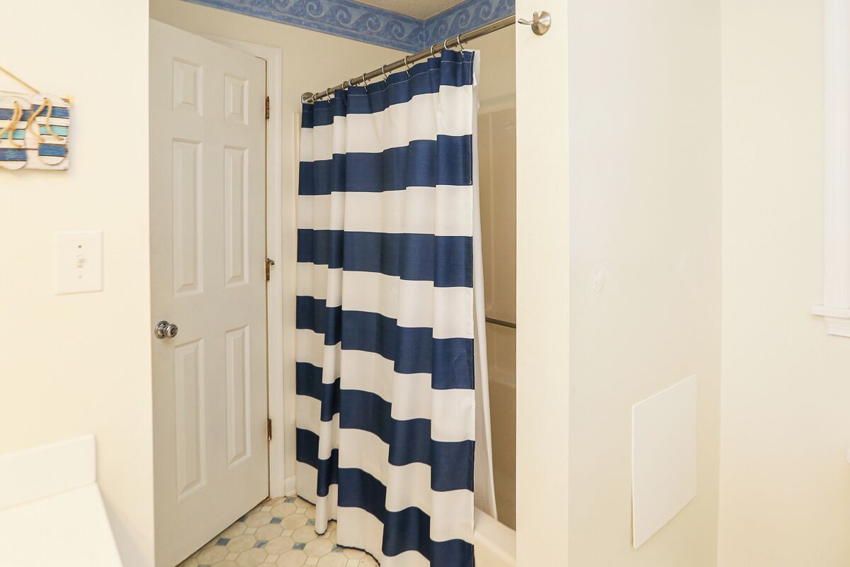A bathroom with a white door, a shower curtain with blue and white stripes, and a tiled floor.