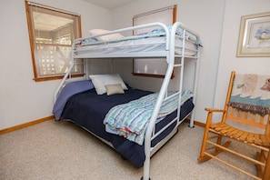 A bunk bed room with a wooden rocking chair, white metal frame, and a window with blinds.