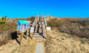 A wooden staircase leading to a beach house with a blue roof, surrounded by sand and vegetation. - Sorrento - Enjoy Sound Views from this Soundside Home w/Private Pool (Southern Shores)