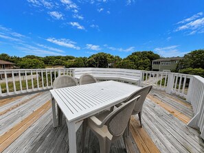 Una terraza con mesa y sillas, rodeada por una barandilla blanca, con vista a una zona residencial.