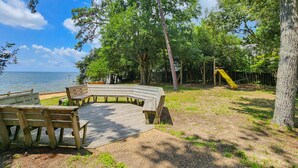 Una terraza de madera con bancos, un parque infantil con un tobogán y vistas al agua.