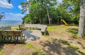 A wooden deck with benches, a playground with a slide, and a view of the water.