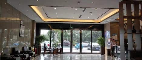 A hotel lobby with a reception desk, seating area, and a view of the street outside.