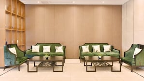 A lobby with two green sofas, a coffee table, and a wooden shelving unit.