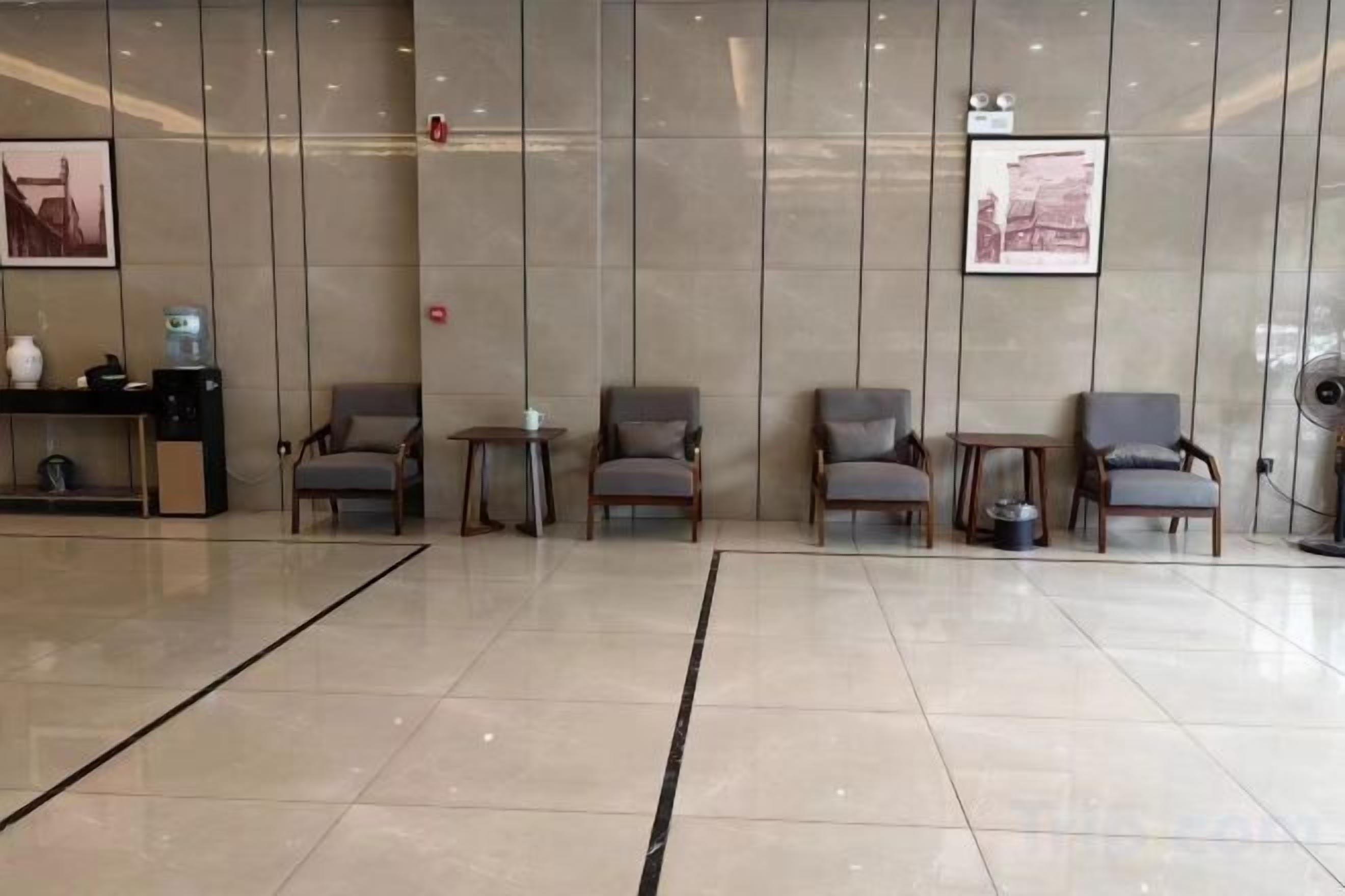 A reception area with a reception desk, several chairs, a small table, and a wall-mounted fan.