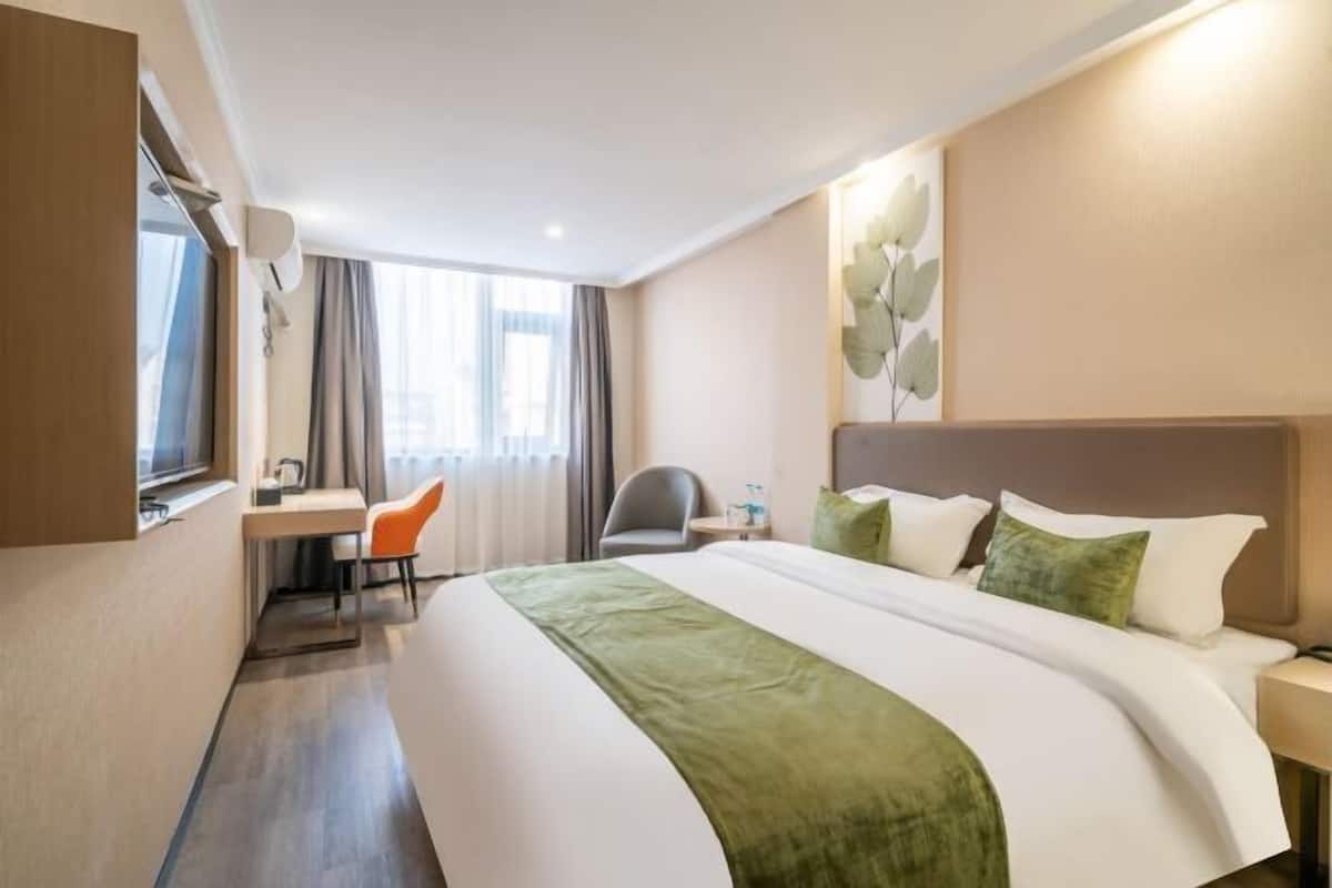 A hotel room with a large bed, a desk, a chair, and a window with curtains.