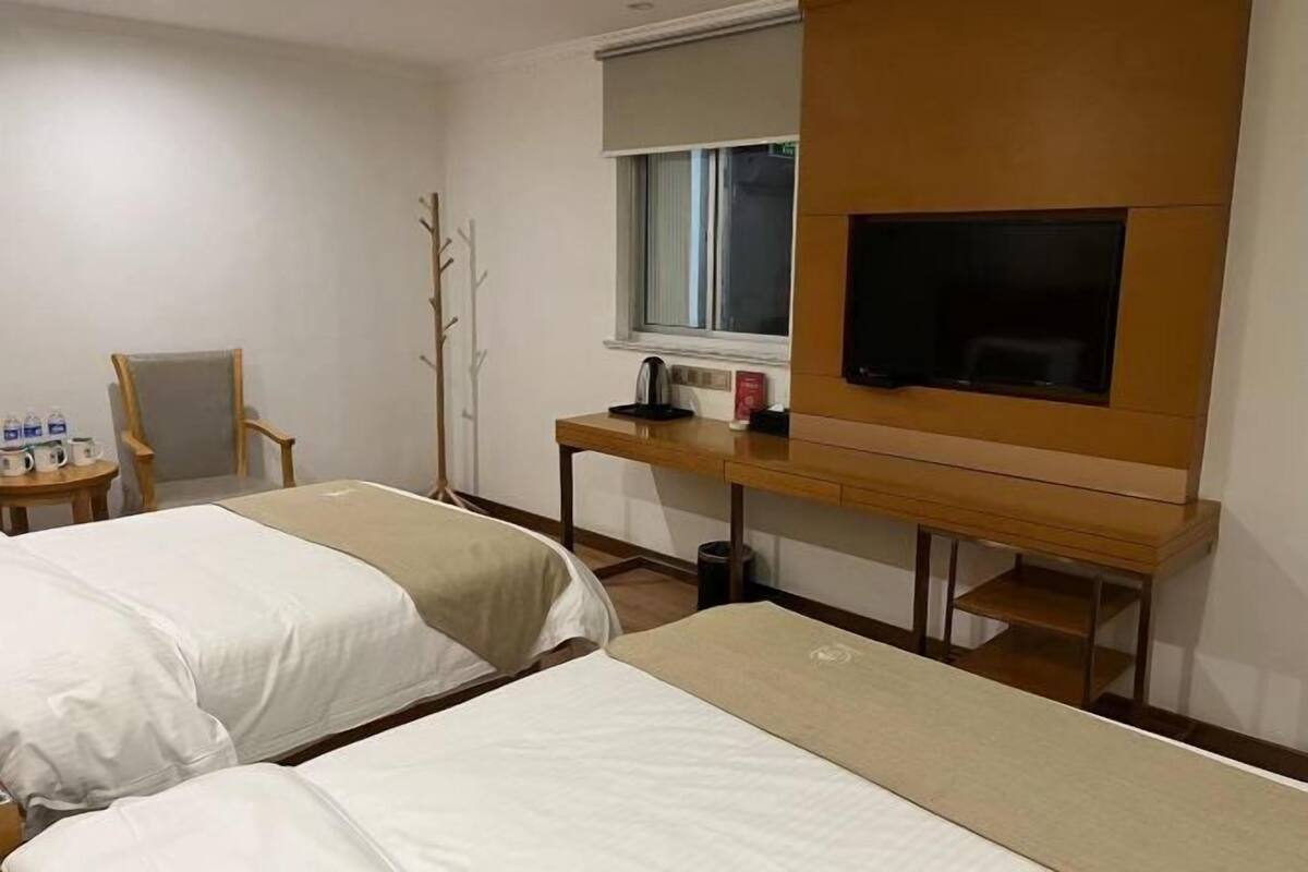 A hotel room with two beds, a TV, a desk with a kettle, and a chair.
