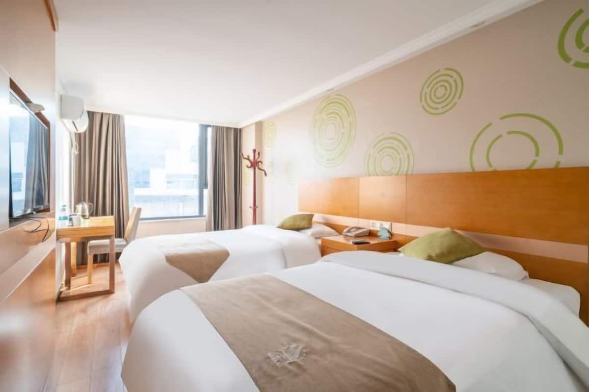 A hotel room with two beds, a desk, a chair, a coat rack, and a window with curtains.