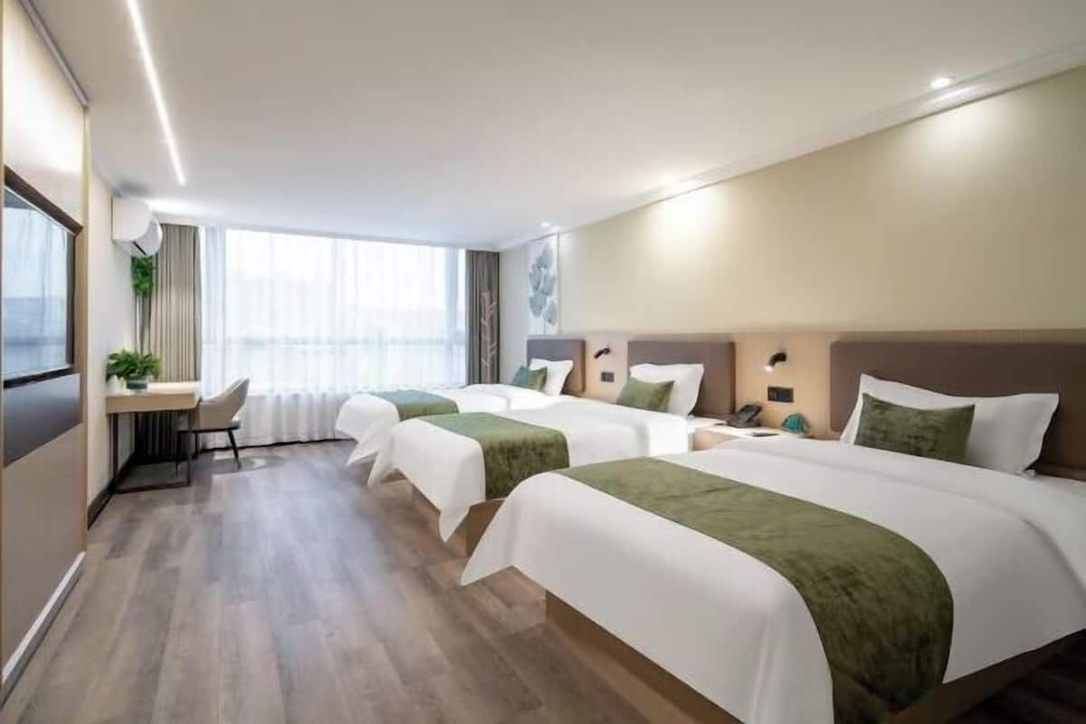 A hotel room with three beds, a desk, and a large window.