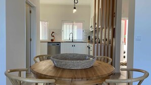 A modern kitchen with white cabinets, a wooden dining table with a woven centerpiece, and a hanging light fixture. - Garajau Apart with Amazing Views, Parking & Wifi. (Caniço)