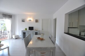 A modern kitchen with white cabinets, a dining table with chairs, and a small TV on a cabinet.