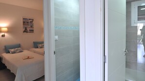 Ein Hotelzimmer mit zwei Betten, einem kleinen Tisch mit einem Buch, einem Wandbild und einer Dusche mit Glastür.