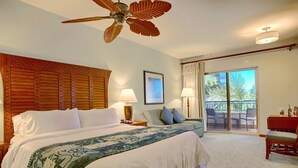 Habitación de hotel con una cama grande, ventilador de techo, balcón con sillas y vistas a palmeras.