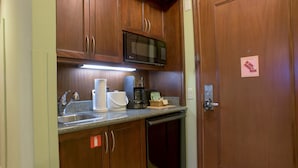 Una kitchenette compacta con armarios de madera, un microondas, una cafetera y un lavamanos.