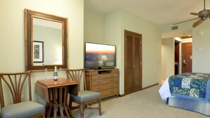 Habitación de hotel con un escritorio de madera, dos sillas, un televisor, un armario y una cama con colcha estampada.