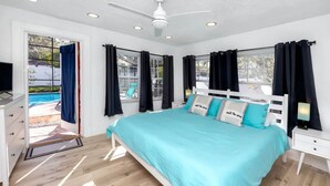 Un dormitorio con cama, escritorio, silla, ventilador de techo y ventana con cortinas.