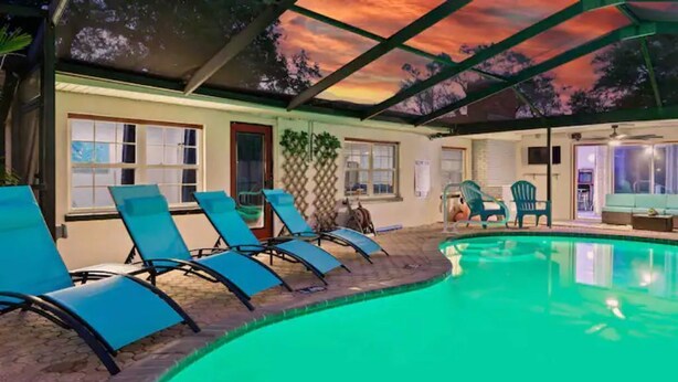 Un área de piscina con sillones de descanso y un porche cubierto.