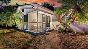 Una casa moderna con cerramiento de vidrio, un sendero y vegetación circundante.