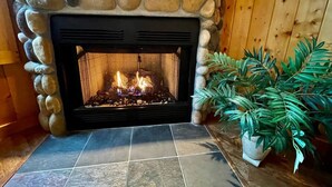 A stone fireplace with a fire, surrounded by a wooden wall and a potted plant. - 19th Hole Chalet - Eagle Crest Resort (Redmond)