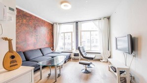 Ett modernt vardagsrum med en soffa, ett soffbord i glas, en svart stol, en gitarr och en tv.
