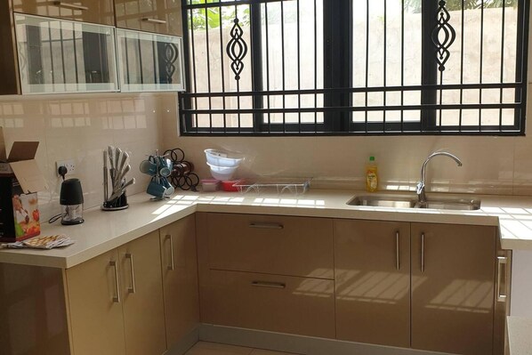 Una cocina con ventana, pileta, alacenas y diversos utensilios.