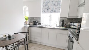 A modern kitchen with white cabinets, a wooden dining table, and a window with a bamboo pattern. - Moor View (Skipton)