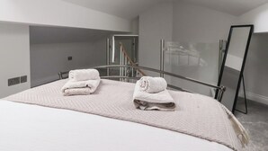 A modern hotel room with a bed, two towels, a glass shower enclosure, and a large mirror. - Moor View (Skipton)