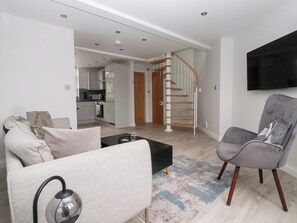 A modern living room with a sofa, a coffee table, and a grey armchair. There is a staircase leading to an upper floor. - Moor View (Skipton)