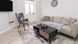 A modern living room with a sofa, a coffee table, a chair, a TV, and a clock on the wall. - Moor View (Skipton)