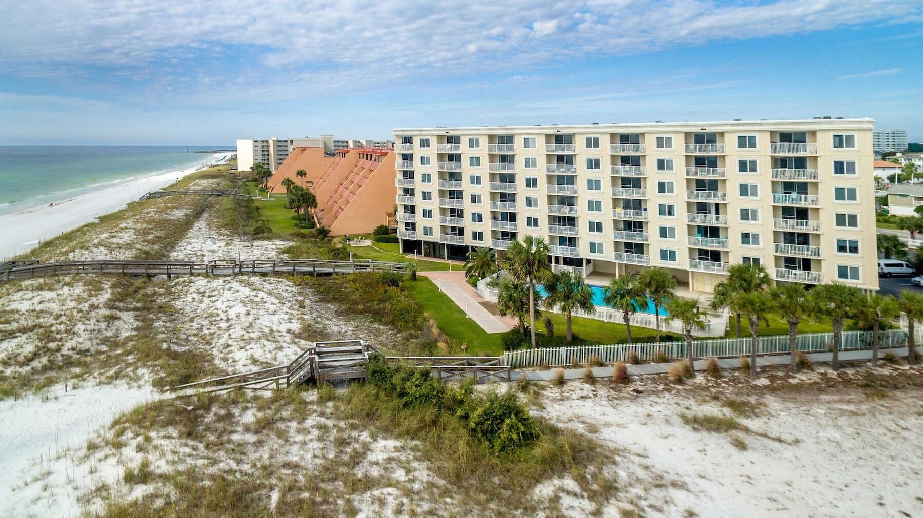 A beachfront hotel with multiple floors, a pool, and a boardwalk leading to the beach.