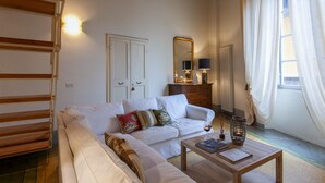 A living room with a sofa, a coffee table, a mirror, and a window with curtains. - Casta Dama Apartment (Lucca)