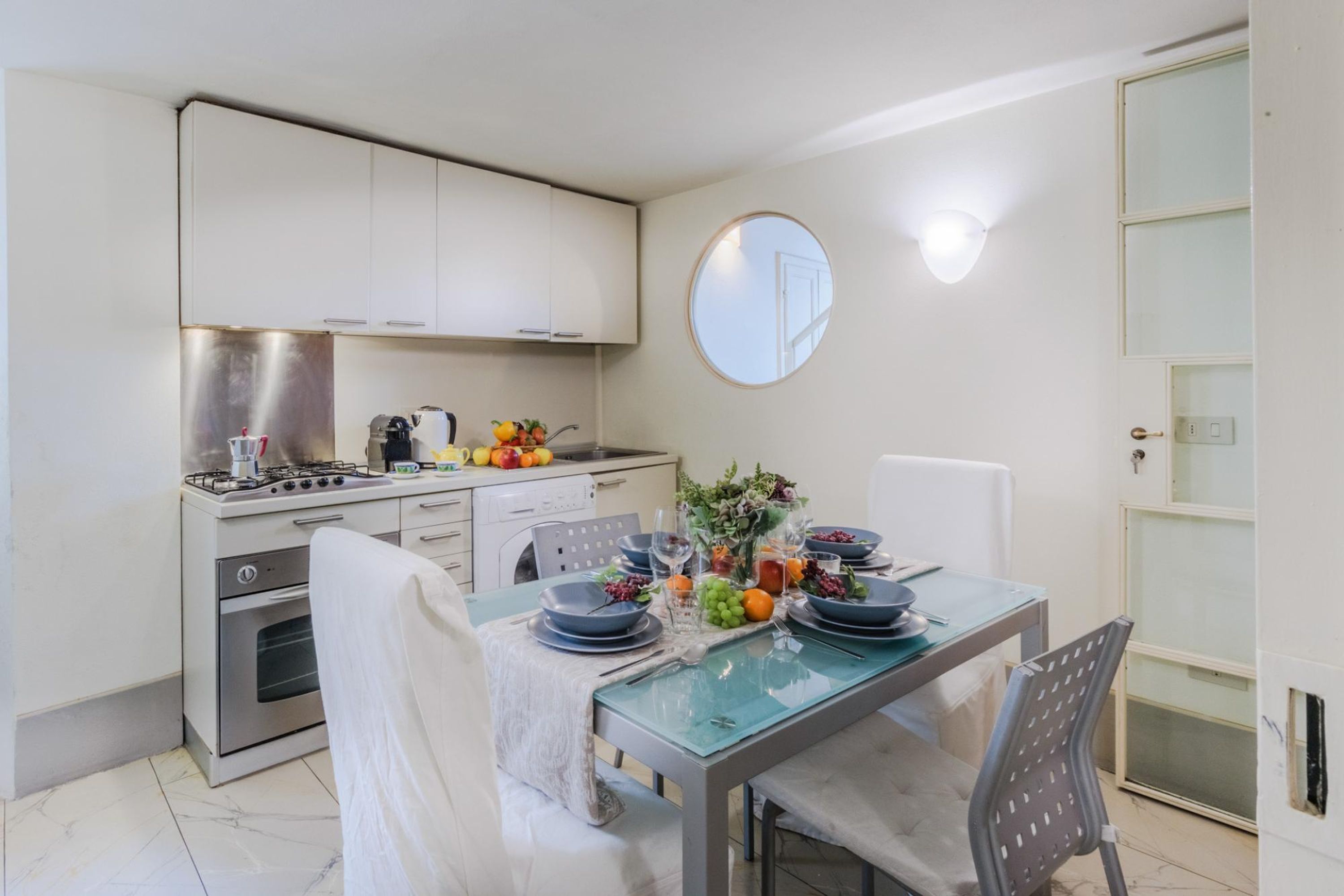 Een moderne keuken met witte kastjes, een roestvrijstalen fornuis en een eettafel gedekt met borden, glazen en fruit.