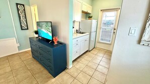 A compact kitchen with white cabinets, a built-in oven, and a sink. A television is mounted on a dark blue cabinet, and a potted plant is on the counter.